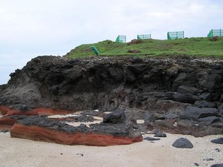 海灘尾端的高地下方，玄武岩石壁因長期受到海水侵蝕而氧化，裸露出鐵銹色的節理