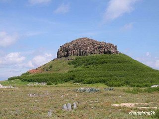 上方是裸露的玄武岩，下方則是綠草和銀合歡包圍著的牛心山